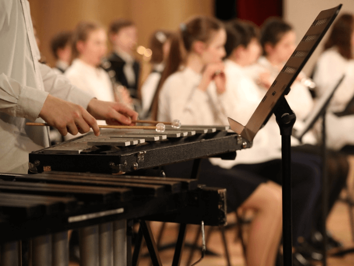 A close up of a child playing the xylophone as part of a school orchestra.