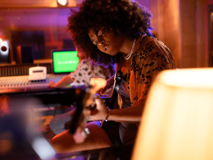 A young, Black female musician, playing electric guitar in a recording studio.
