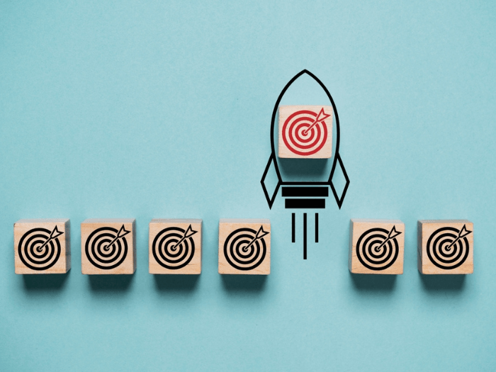 A red dartboard painted on a wooden block with the outline of a rocket launching upwards. Next to it are other wooden blocks with black targets.