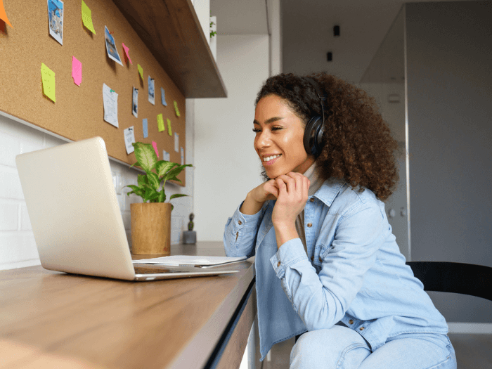 Young Black Woman wearing headphones and smiling at an open laptop.