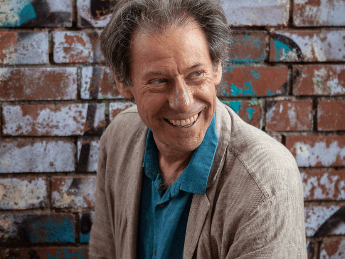 Portrait of John Wallace, stood smiling against a brick wall.