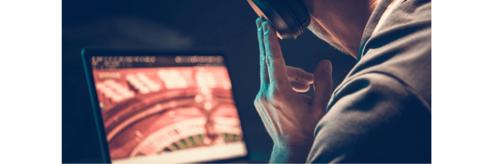 Man with his hand on his ear, listening carefully to music through his over ear headphones, in front of an open laptop.
