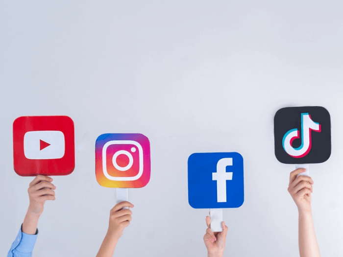 Four hands holding up signs of logos: YouTube, Instagram, Facebook and TikTok.