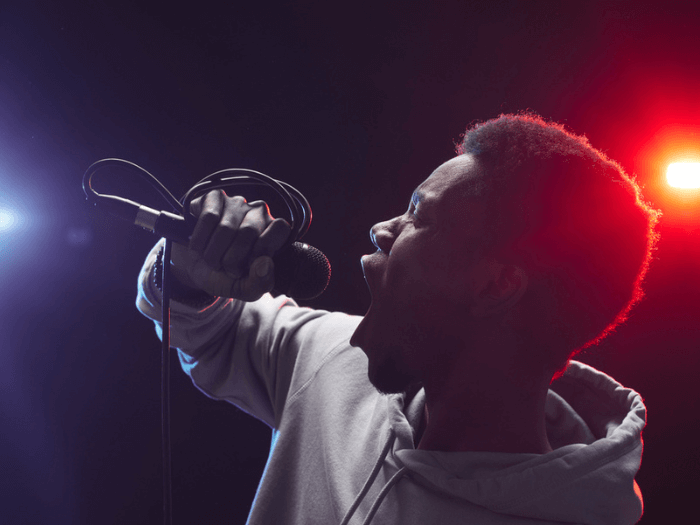 Young Black male musician, singing into a microphone against a bright studio light.