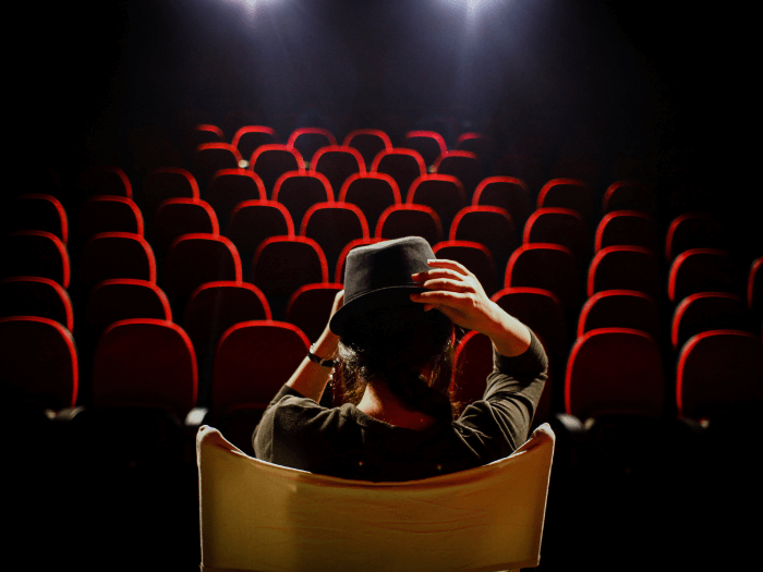 Young woman on director's chair on stage, in front of empty theatre seats.