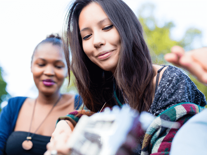 Two young female musicians sat outside, one playing acoustic guitar.